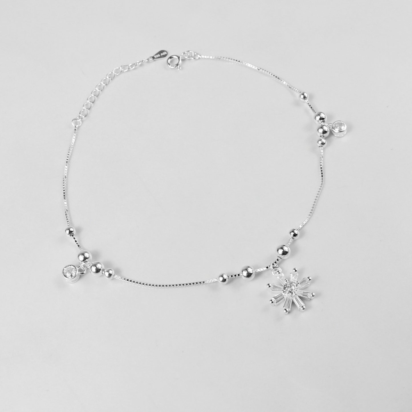 The 'Floral Charm' anklet, crafted from 925 sterling silver, featuring a graceful chain adorned with intricate floral-inspired charms for a touch of elegance.