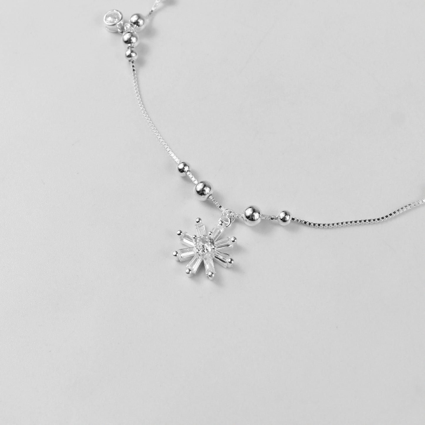 The 'Floral Charm' anklet, crafted from 925 sterling silver, featuring a graceful chain adorned with intricate floral-inspired charms for a touch of elegance.