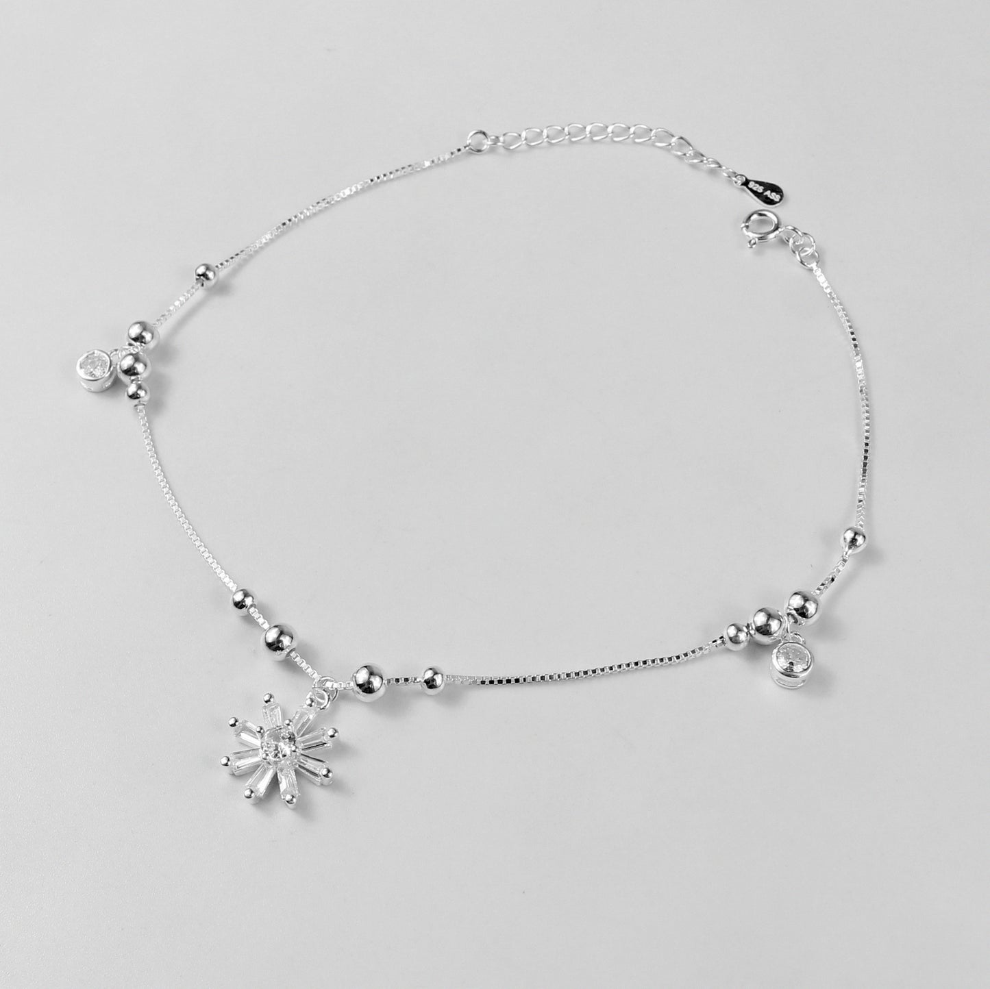 The 'Floral Charm' anklet, crafted from 925 sterling silver, featuring a graceful chain adorned with intricate floral-inspired charms for a touch of elegance.