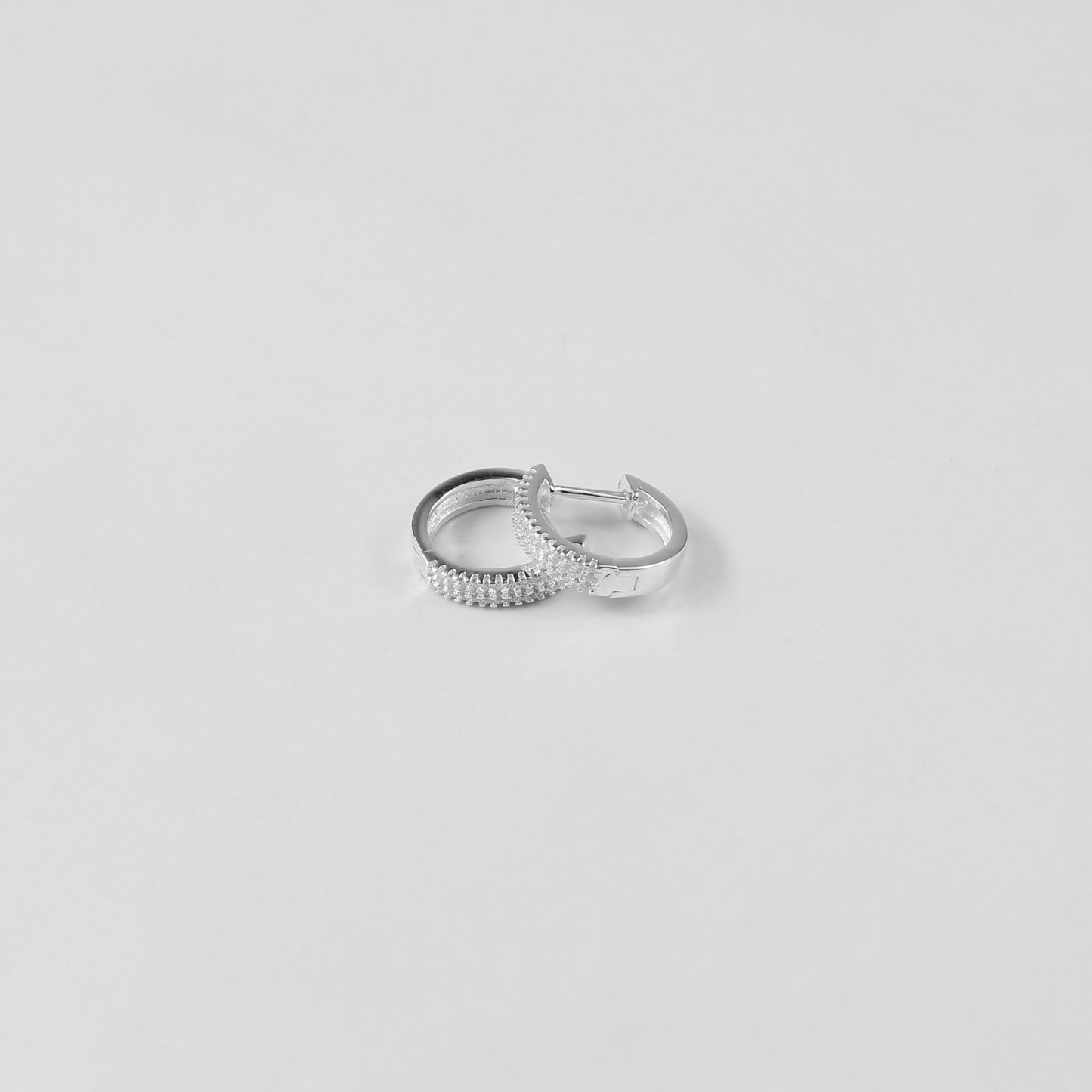 Minimalist sterling silver ear studs labeled 'Radiant Glow,' their polished finish and glittering crystal detailing highlight modern sophistication, placed on a velvet backdrop.