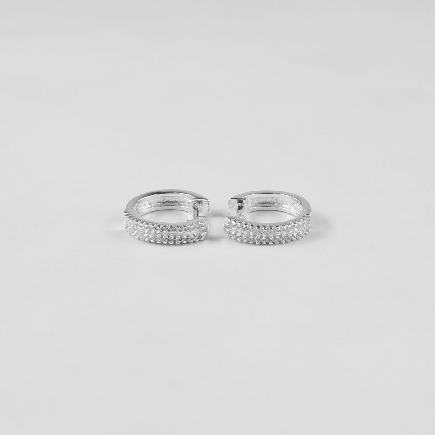 Minimalist sterling silver ear studs labeled 'Radiant Glow,' their polished finish and glittering crystal detailing highlight modern sophistication, placed on a velvet backdrop.