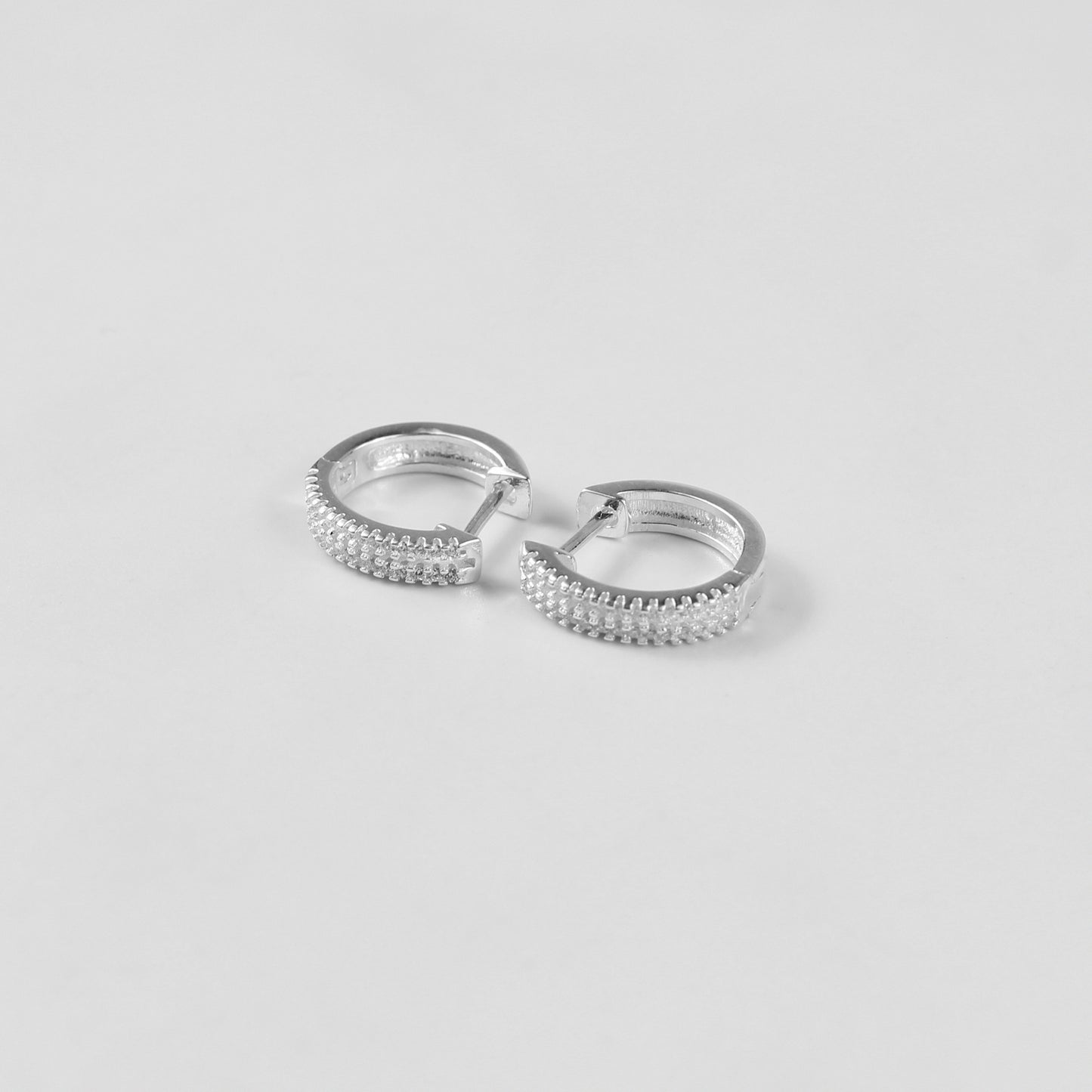 Minimalist sterling silver ear studs labeled 'Radiant Glow,' their polished finish and glittering crystal detailing highlight modern sophistication, placed on a velvet backdrop.