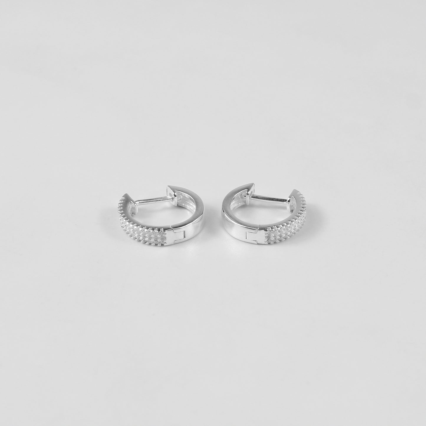 Minimalist sterling silver ear studs labeled 'Radiant Glow,' their polished finish and glittering crystal detailing highlight modern sophistication, placed on a velvet backdrop.