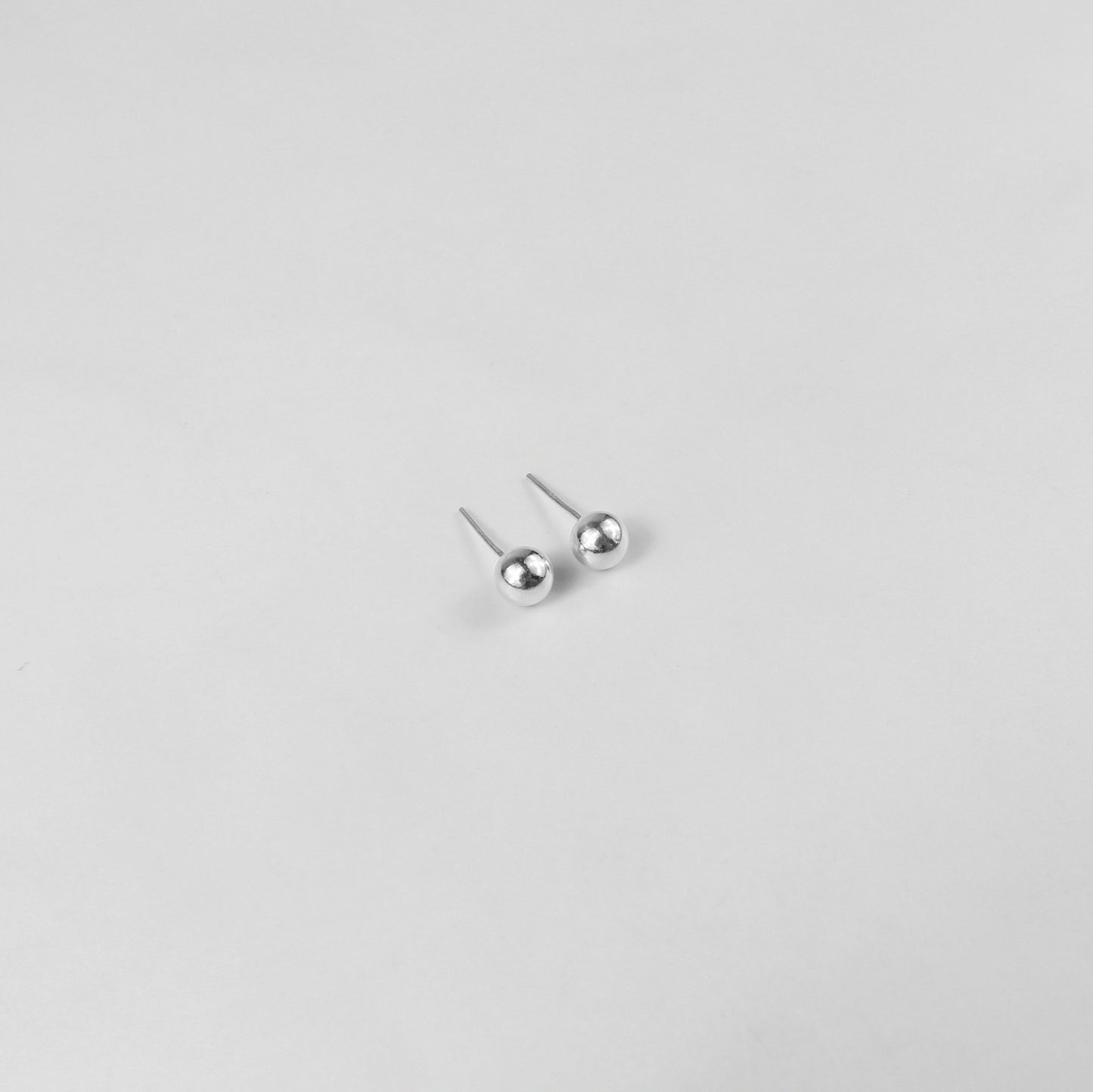 Sterling silver ear studs shaped like perfect spheres, displayed on a white marble background. Their polished texture creates a luxurious and timeless appeal.