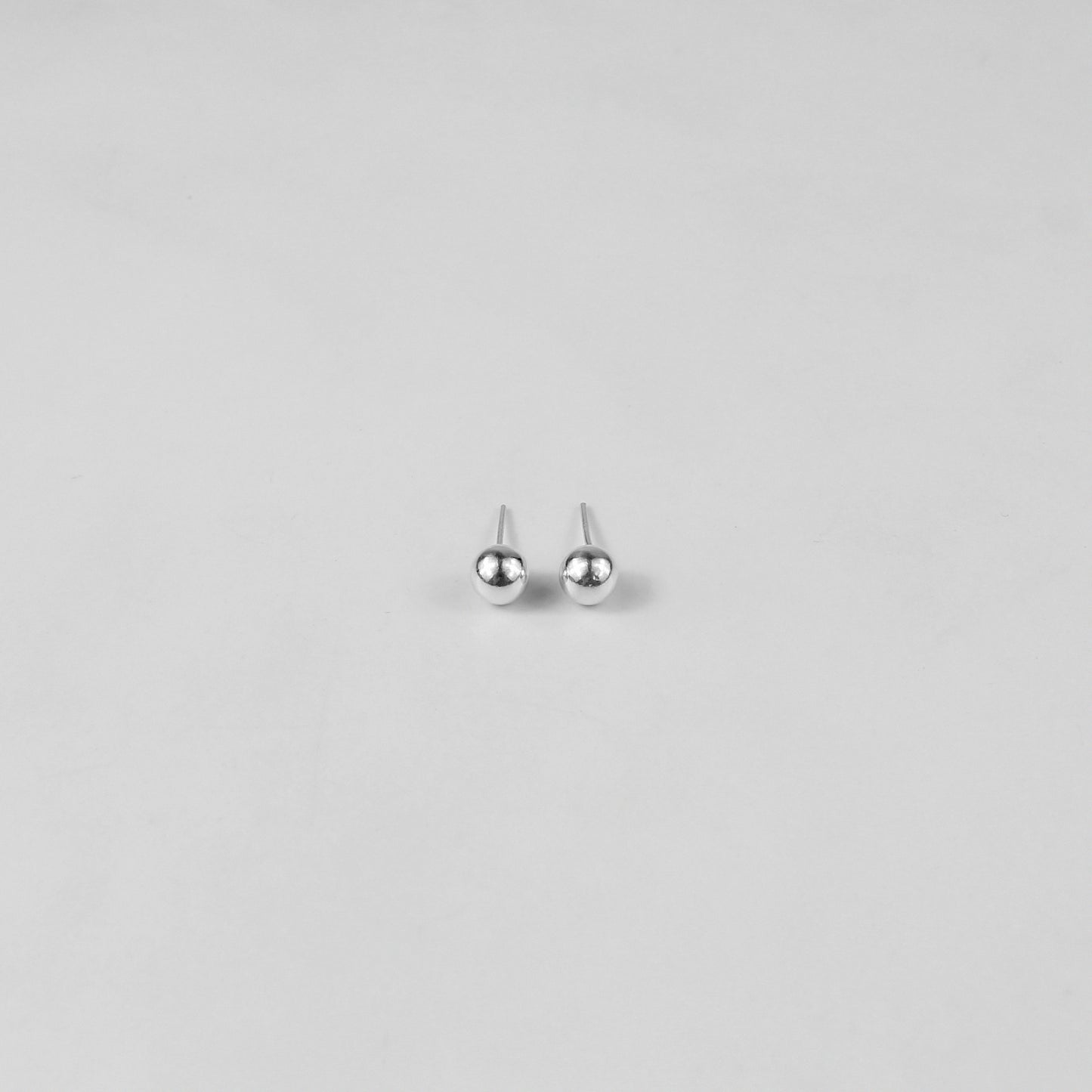 Sterling silver ear studs shaped like perfect spheres, displayed on a white marble background. Their polished texture creates a luxurious and timeless appeal.