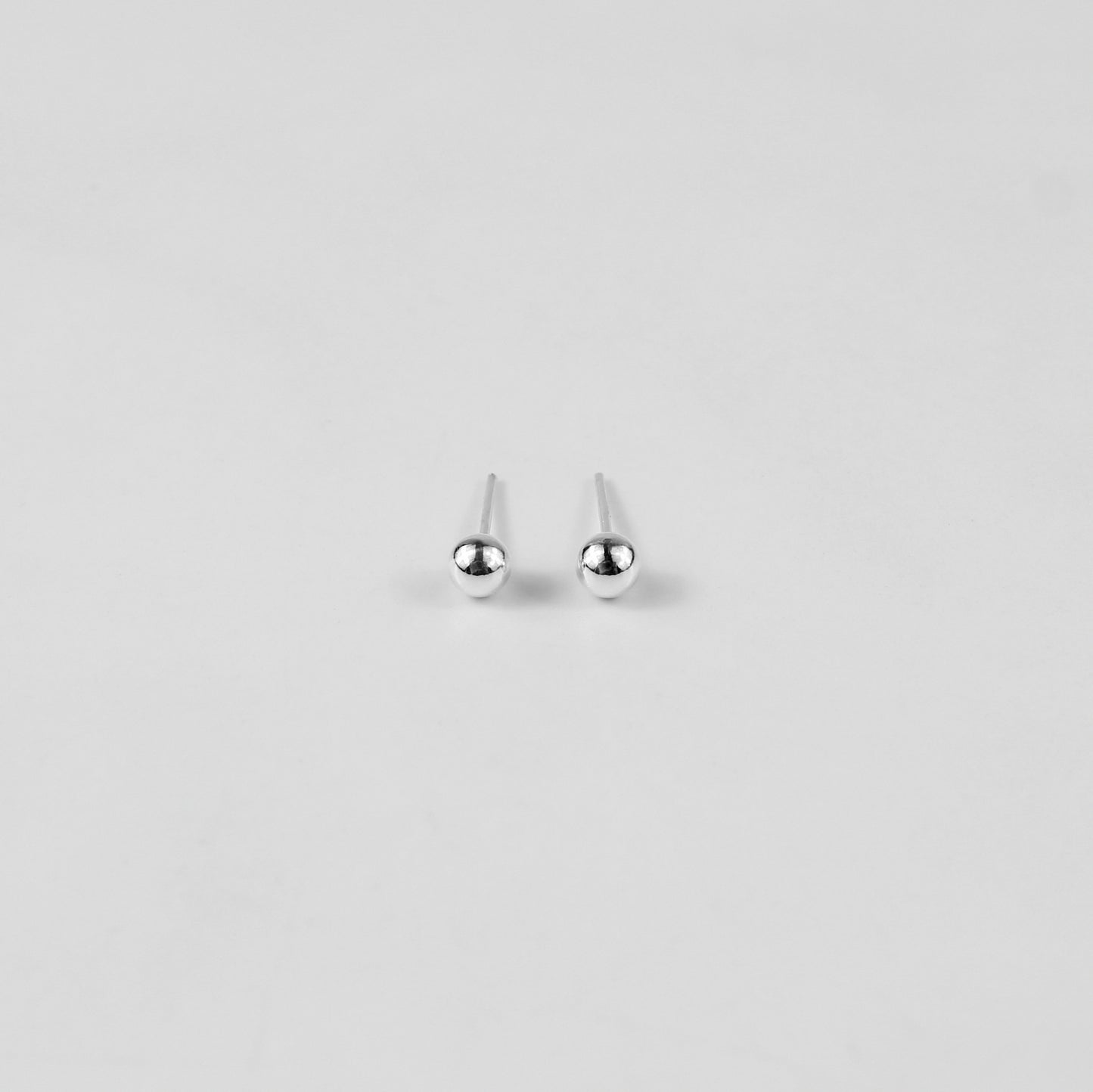 Sterling silver ear studs shaped like perfect spheres, displayed on a white marble background. Their polished texture creates a luxurious and timeless appeal.
