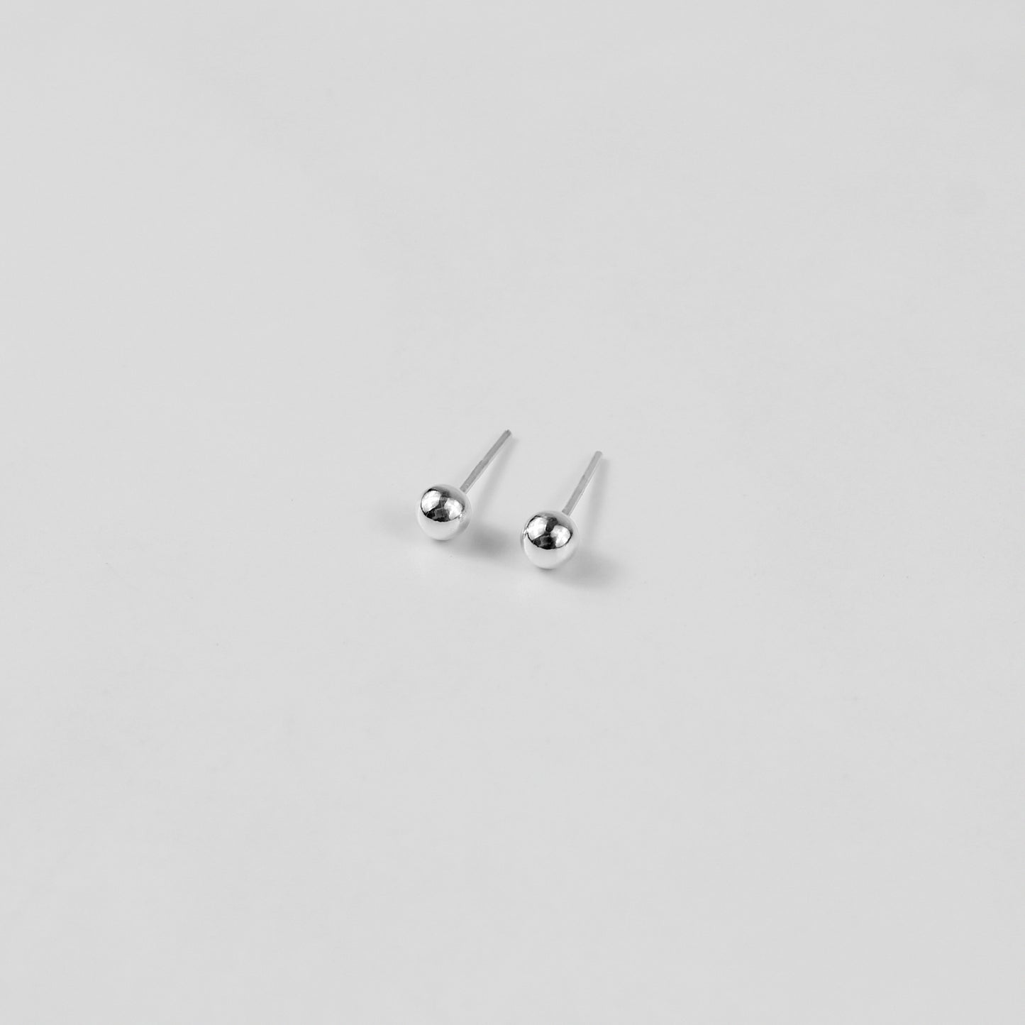 Sterling silver ear studs shaped like perfect spheres, displayed on a white marble background. Their polished texture creates a luxurious and timeless appeal.