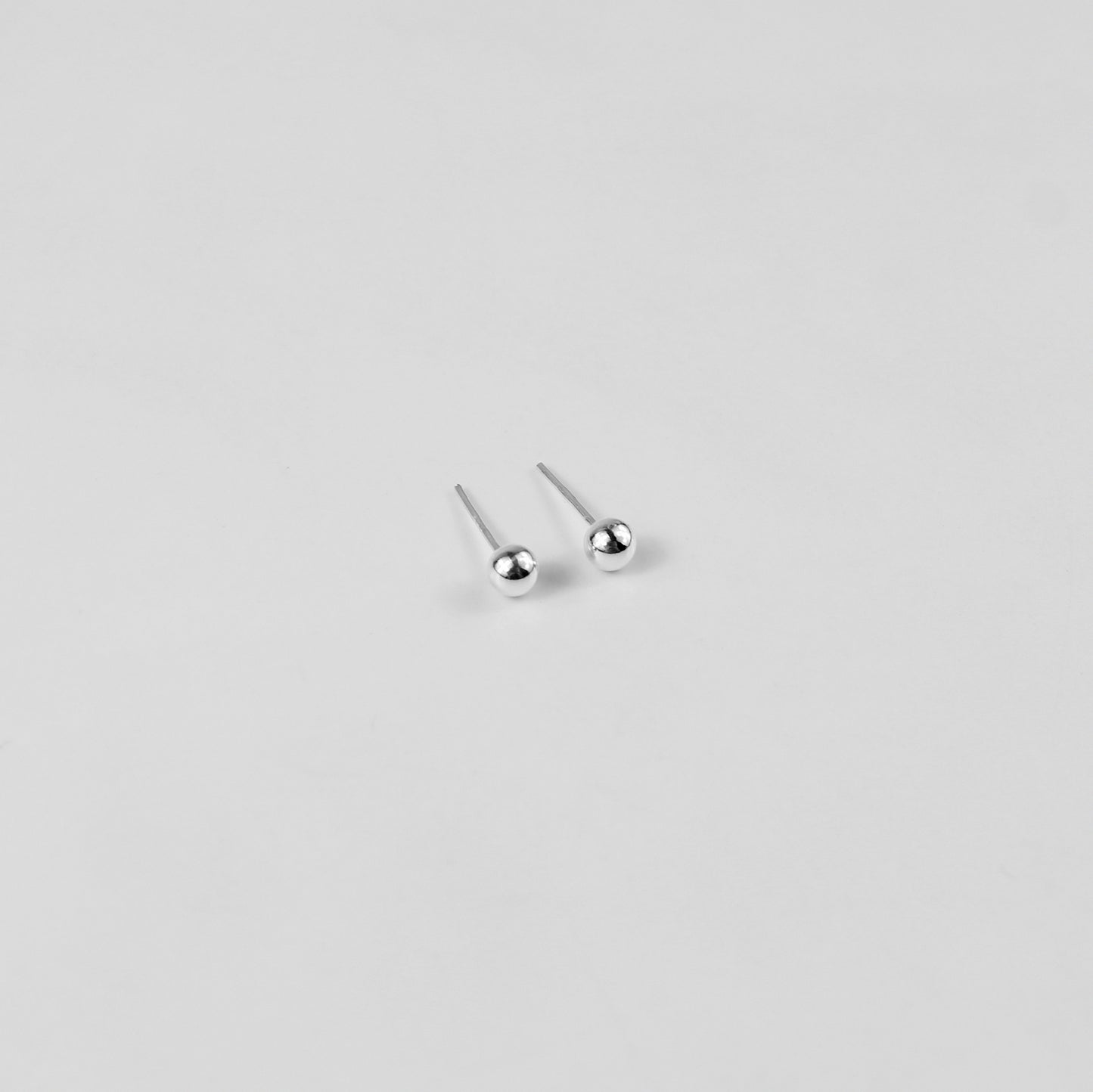 Sterling silver ear studs shaped like perfect spheres, displayed on a white marble background. Their polished texture creates a luxurious and timeless appeal.