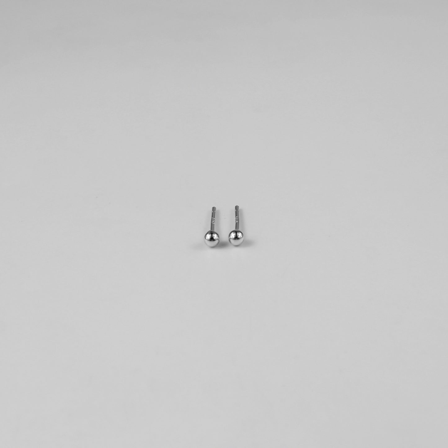 Sterling silver ear studs shaped like perfect spheres, displayed on a white marble background. Their polished texture creates a luxurious and timeless appeal.