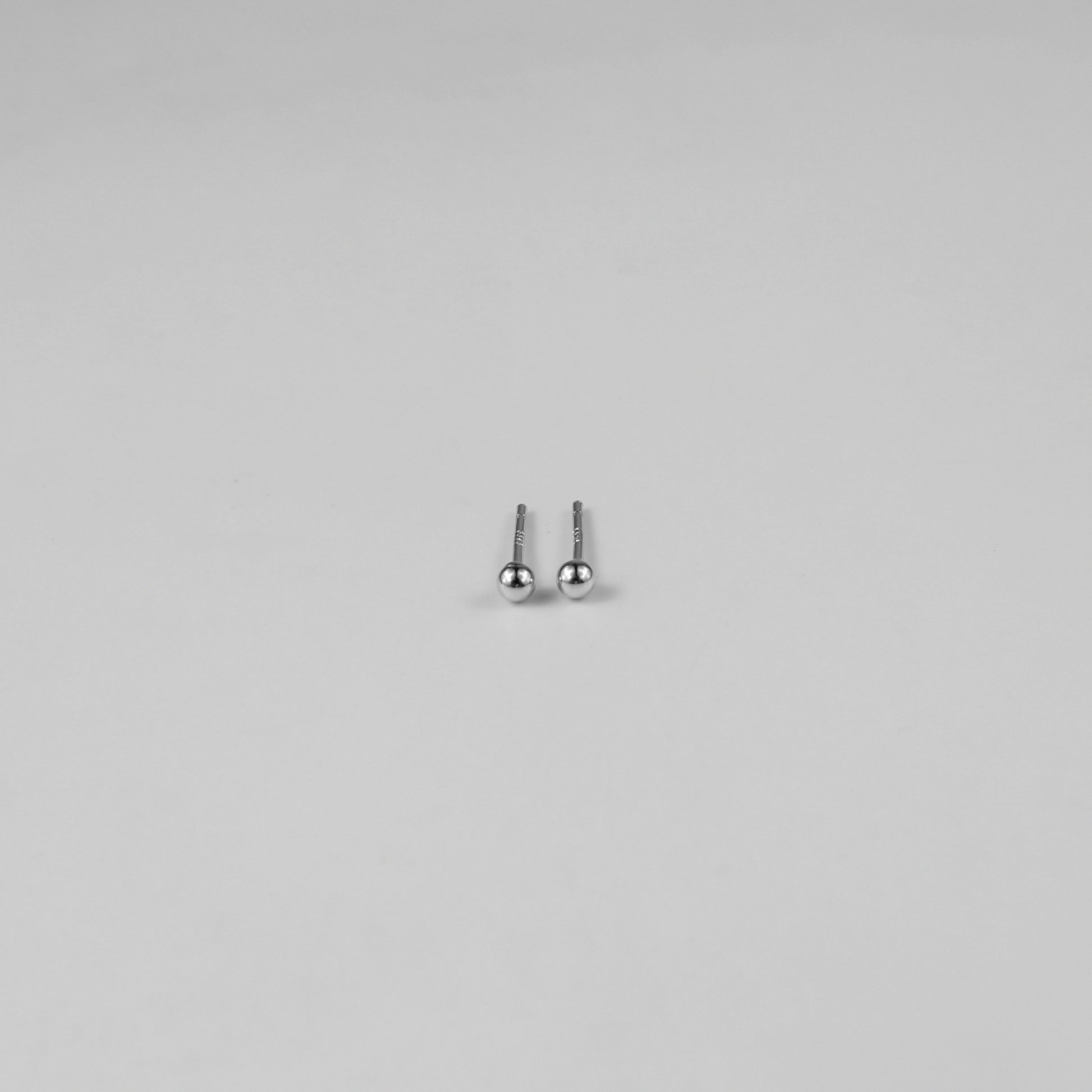 Sterling silver ear studs shaped like perfect spheres, displayed on a white marble background. Their polished texture creates a luxurious and timeless appeal.