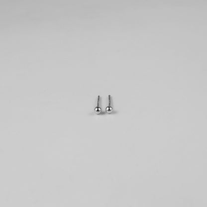 Sterling silver ear studs shaped like perfect spheres, displayed on a white marble background. Their polished texture creates a luxurious and timeless appeal.