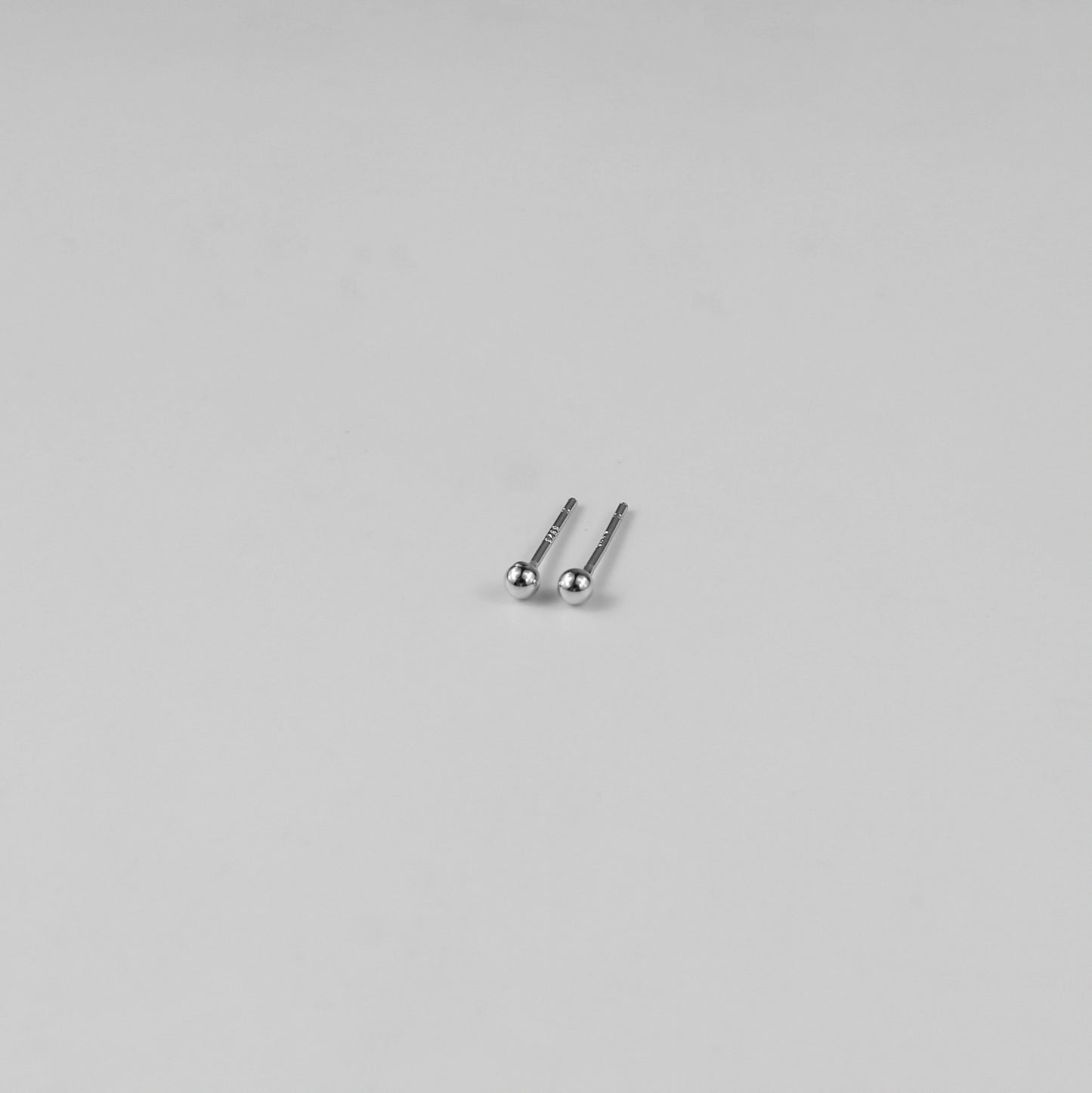 Sterling silver ear studs shaped like perfect spheres, displayed on a white marble background. Their polished texture creates a luxurious and timeless appeal.