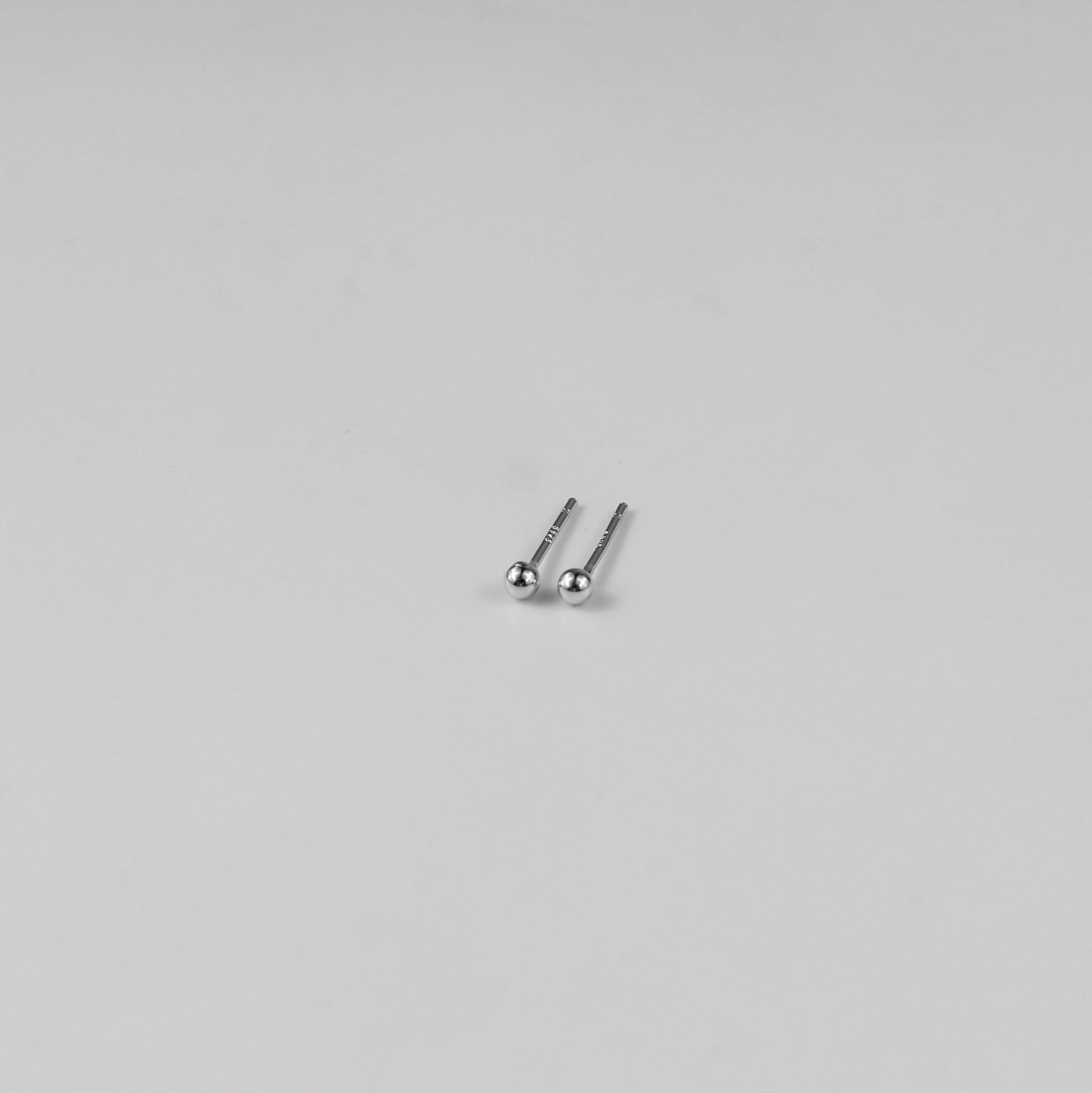 Sterling silver ear studs shaped like perfect spheres, displayed on a white marble background. Their polished texture creates a luxurious and timeless appeal.