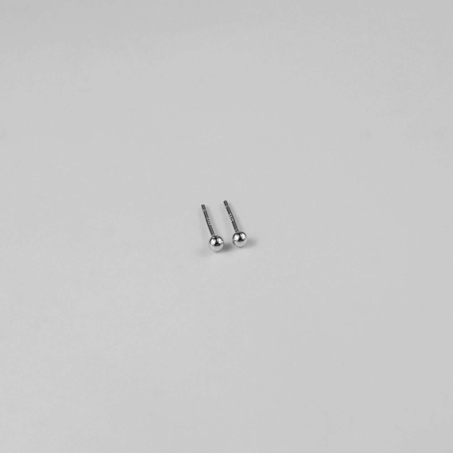 Sterling silver ear studs shaped like perfect spheres, displayed on a white marble background. Their polished texture creates a luxurious and timeless appeal.