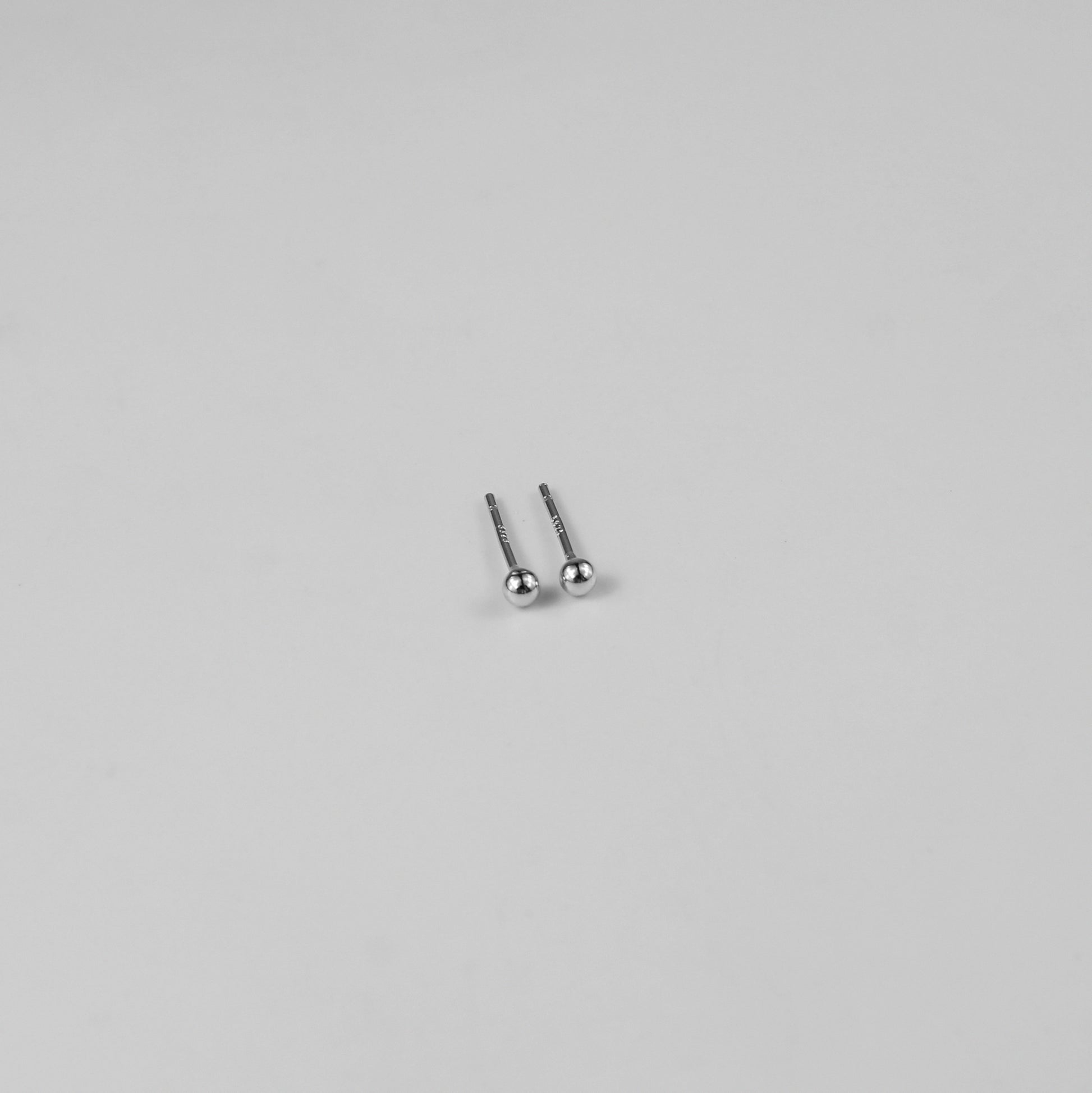 Sterling silver ear studs shaped like perfect spheres, displayed on a white marble background. Their polished texture creates a luxurious and timeless appeal.