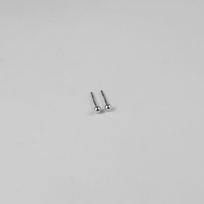 Sterling silver ear studs shaped like perfect spheres, displayed on a white marble background. Their polished texture creates a luxurious and timeless appeal.