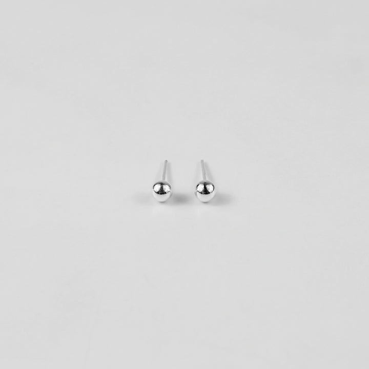 Sterling silver ear studs shaped like perfect spheres, displayed on a white marble background. Their polished texture creates a luxurious and timeless appeal.